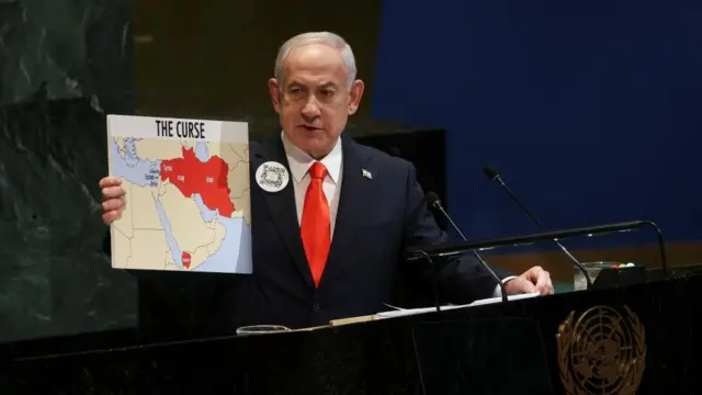Netanyahu holds a board which says 'The curse' which shows a map of Syria, Iraq and Iran coloured in red