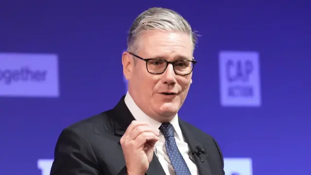 A headshot of Keir Starmer as he delivers his speech. He stands against a purple background which is slightly blurred