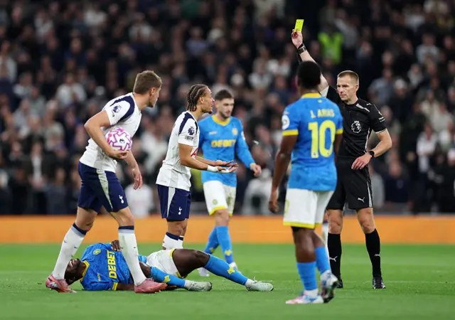 Match referee Michael Salisbury shows a yellow card to Xavi Simons