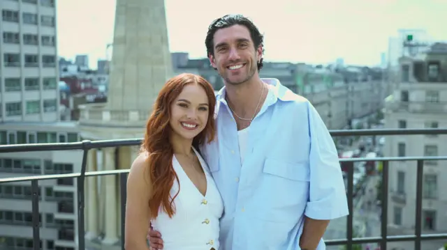 Alexis Warr on the left and Julian Caillon on the right. there are standing on the balcony of the BBC Broadcasting House, with the background of Regent Street behind them. Warr is wearing a white waistcoat and Caillon is wearing a light blue, half buttoned, short sleeved shirt.