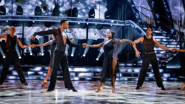 A group of men and women wearing black link hands and dance on the set of Strictly.