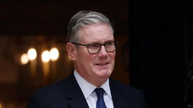 Keir Starmer walks through the door of Number 10 wearing a dark suit and tie.