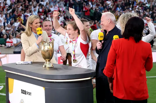 Abby Dow of England celebrates with pundits and the Women's Rugby World Cup Trophy