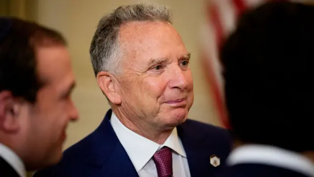 Steve Witkoff in a blue suit jacket with white shirt and red/purple tie. He is smiling but looking to the side of the camera.