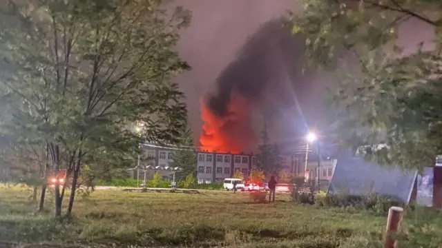 A building on fire in the distance with smoking billowing into the air