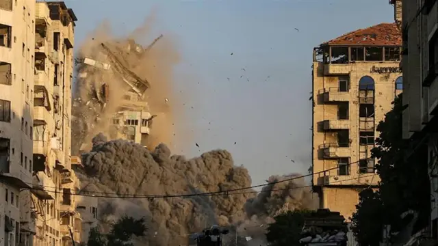 A tower moments after a strike beginning to collapse with a large plume of smoke at its base