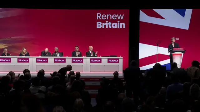 Wide shot of stage at Labour party conference, with Foreign Secretary Yvette Cooper speaking at the lectern.