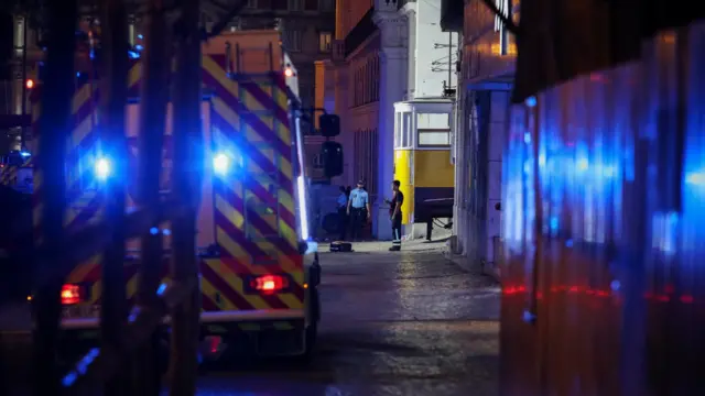 Ambulance parked in the Lisbon street with two officers and an onlooker standing in front of it.