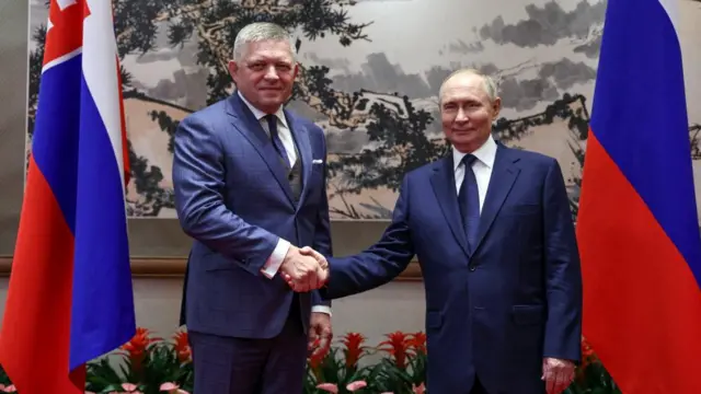 Putin shaking hands with Fico in front of their countries' flags