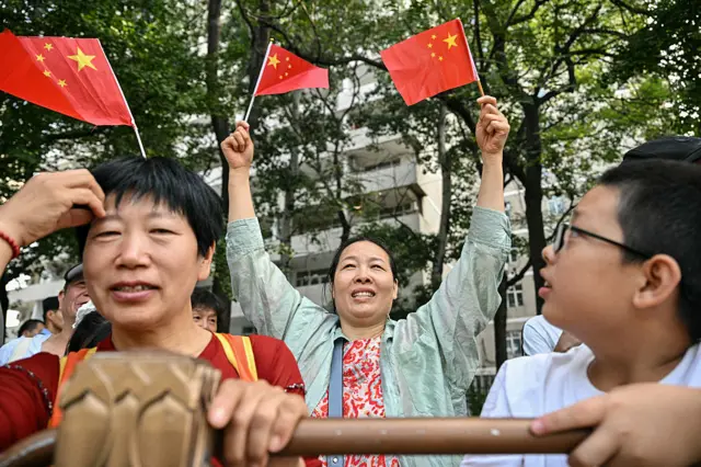 A lady waves two Chinese flags in the air among spectators