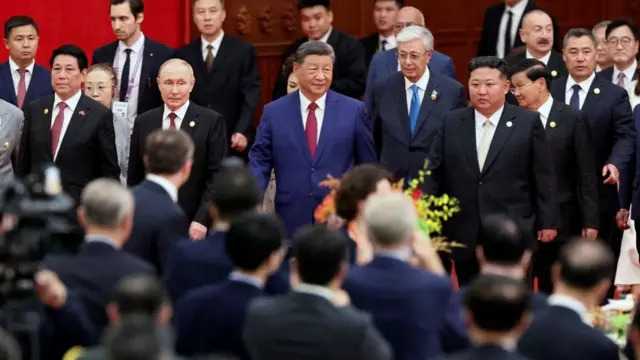 Xi Jinping arrives at a reception, flanked by Putin and Kim Jong Un