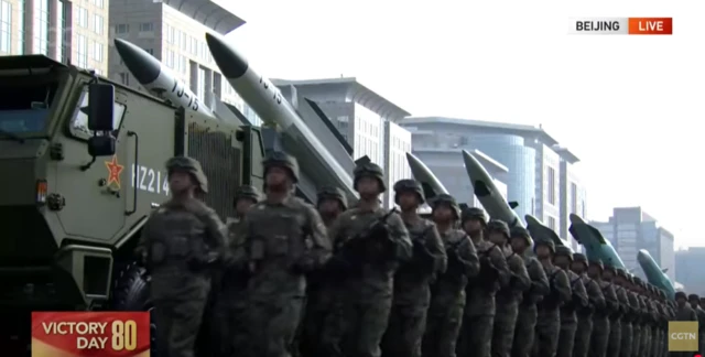 Front view of soldiers running past military vehicles