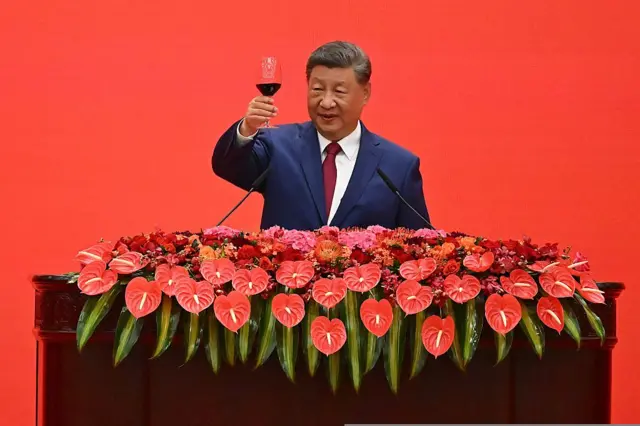 China's President Xi Jinping gives a toast with a glass of red wine on a podium covered with red flowers
