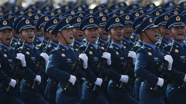 Five lines of Chinese troops march in navy suits, holding their guns