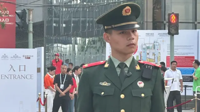 A soldier stands at a road junction, with people in the background