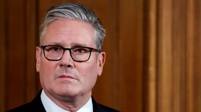 Starmer in front of a wooden background with a black suit