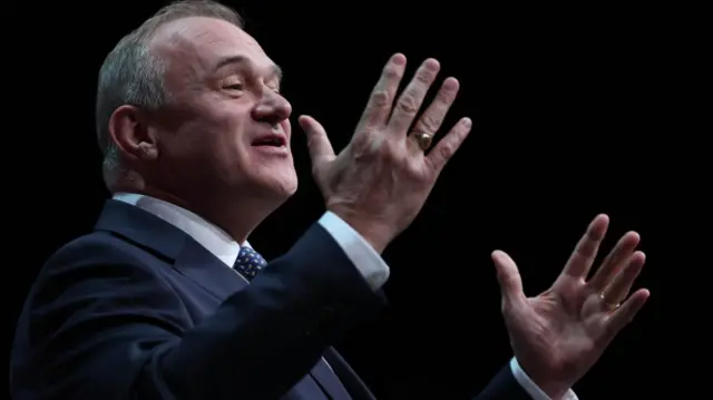 Ed Davey, wearing a suit, speaks on stage