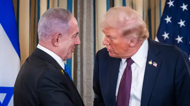 Benjamin Netanyahu (L) shakes hands with Donald Trump (R) ahead of a press conference inside the White House. They're both wearing dark suits and an Israeli flag is visible to the left of the frame