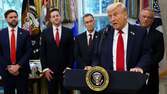 Trump speaks at a podium with members of his team standing behind him
