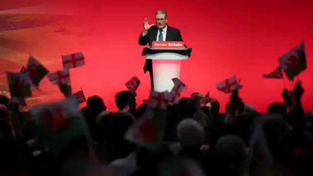 Prime Minister Keir Starmer delivers his keynote speech at Britain's Labour Party in front of flags held up by audience