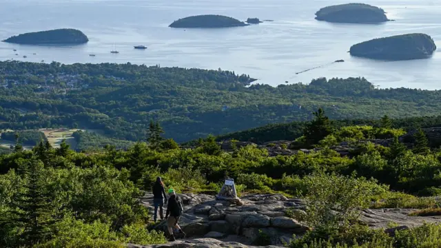 Acadia National Park, with hikers seen on a mountain, and islands off the coast in the distance