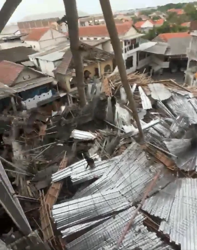A screengrab of a video showing a collapsed roof filmed from above, corrugated iron, concrete, steel bars and other construction materials covering the ground