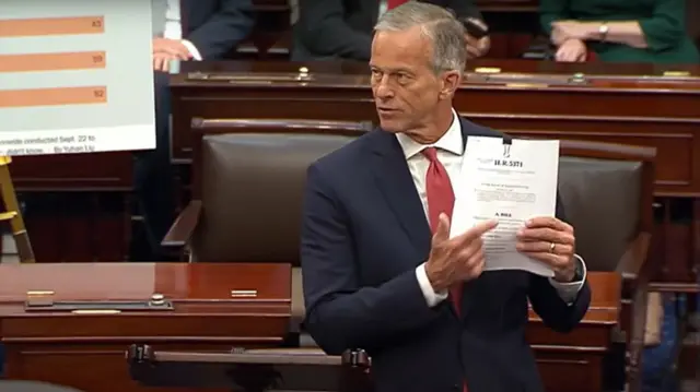 John Thune holds up a white document containing the Republican proposal