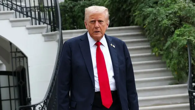 Donald Trump on lawn of White House, wearing suit with red tie.