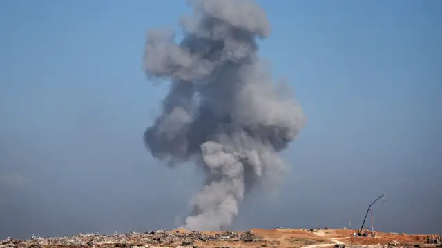 A landscape shot of a large plume of smoke rising from skyline