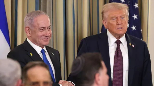 Donald Trump and Netanyahu wearing suits and shaking hands.