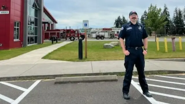 William Cridge stands in a fire station parking lot wearing a blue uniform