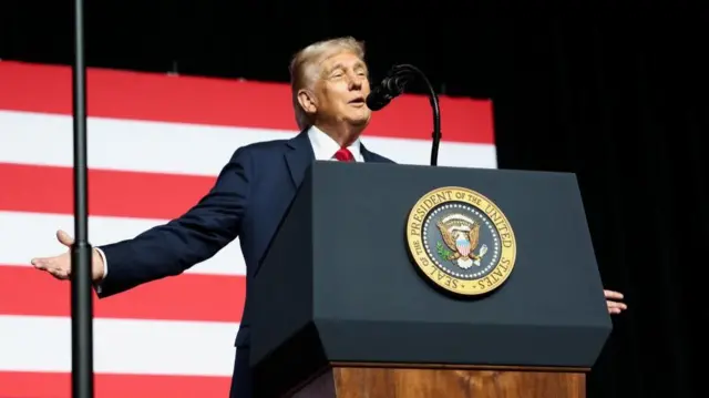 President Trump in a blue jacket in front of the red and white stripes of an American flag