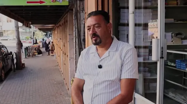 Nasr Al-Husseini stands outside a shop door and speaks