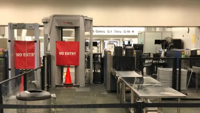 A closed down security airport checkpoint which shows the security belt and the body scanner, which has a large red no entry banner across it and a traffic cone in front of it. The area is empty