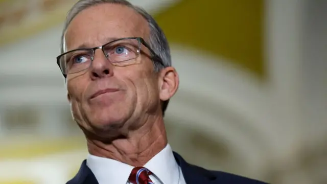 Senator John Thune wears glasses, a red tie and a blue suit jacket