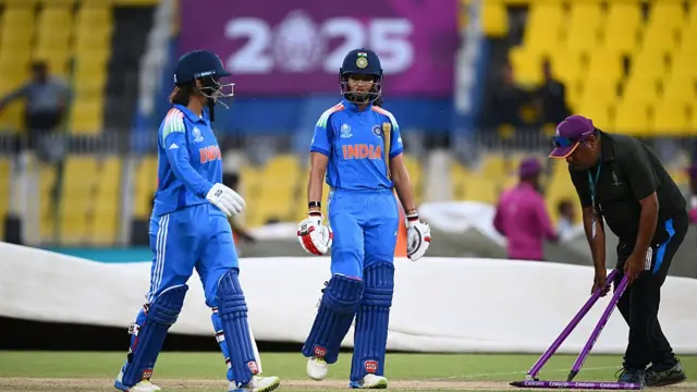 Pratika Rawal of India leaves the field with team mate Harleen Deol as play is delayed due to rain