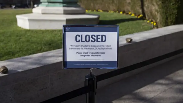 A blue closed sign in front of a wall and a garden