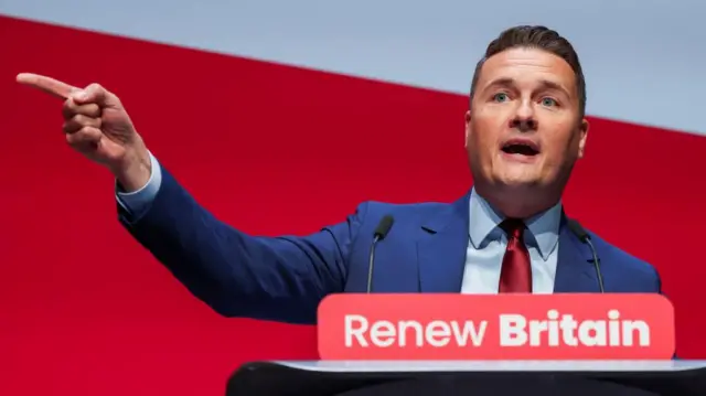 Wes Streeting points to the left as he speaks at the lectern which bears the words 'renew Britain'