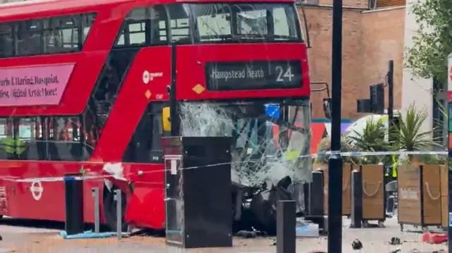 red London bus seems to be on pavement, with smashed windscreen and police cordon