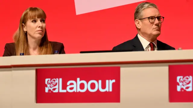 Angela Rayner and Keir Starmer, Prime Minister sit next to one another at a desk emblazoned with the Labour Party logo