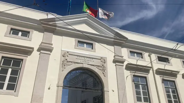 The exterior of the Santa Casa da Misericórdi building - a grand white structure with an archway entrance and flying the Portuguese flag above the roof