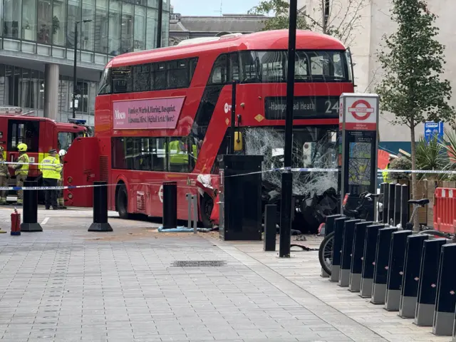 a red London bus with a damaged windscreen following the crash