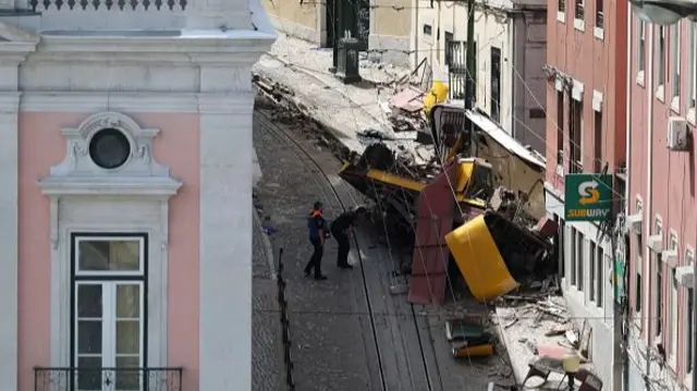 A small cobbled street with pink houses lining the street, and the wreckage of the yellow fenicular piled high