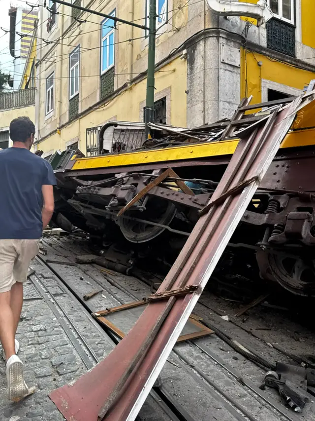 A man stands next to the wreck of a funicular carriage in Lisbon.