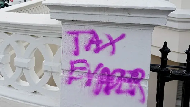 A landscape image showing the phrase 'tax evader' painted in pink on a white wall