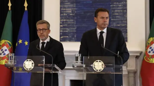 The two men speak at lecterns next to each other at a news conference - both wearing black suits and black ties.