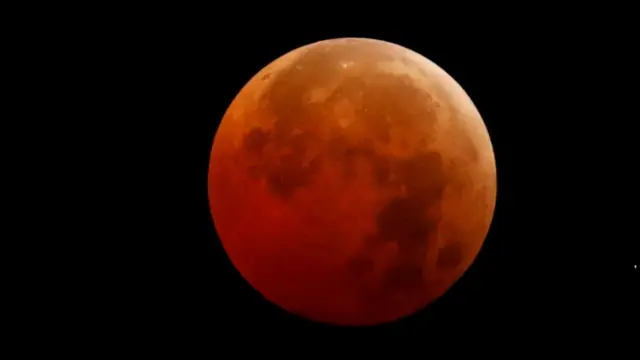 A red/orange hued moon in a black sky.