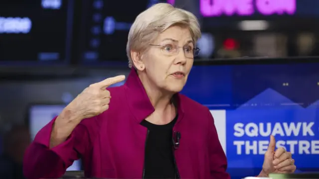 Elizabeth Warren speaks. She is wearing a purple sweater over a black shirt