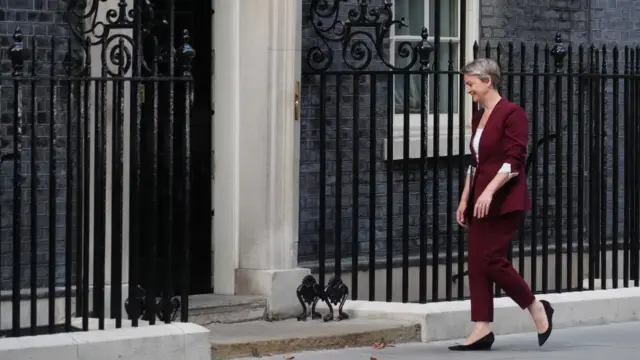 Woman in maroon suit walks towards a blank front door