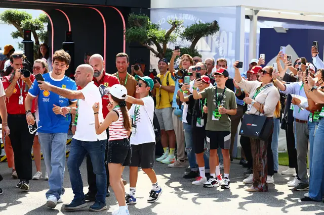Ferrari's Charles Leclerc poses for a selfie with fans at the Italian Grand Prix, with many people taking pictures of him